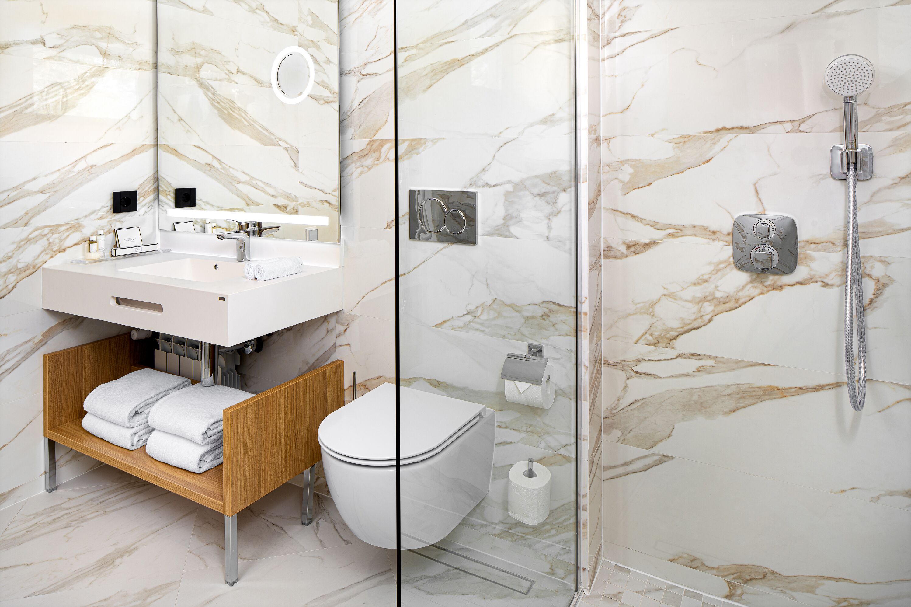 Un baño moderno con salpicadero de mármol, ducha con cerramiento de vidrio, lavamanos blanco y tocador de madera.