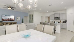 A modern kitchen with white cabinets, a microwave, and a dining area with a marble table and chairs. - Luxury Family Villa in Solterra with Pool, Spa & Games Room Near Disney (Davenport)