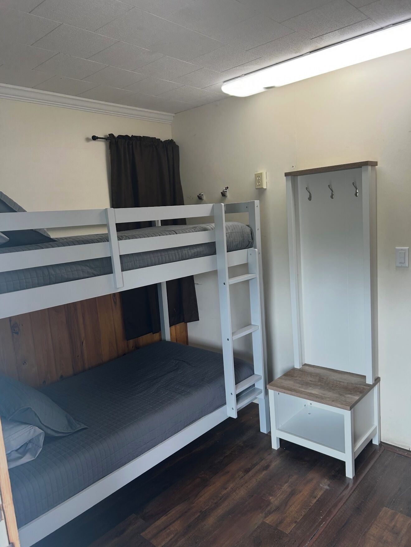 A bunk bed room with a wooden floor, a white wardrobe, and a ceiling light.