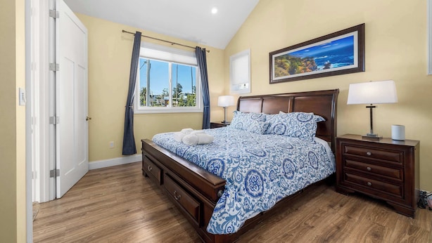 Un dormitorio con cama de madera, una mesita de noche, un aparador, una ventana con cortinas y un cuadro en la pared.