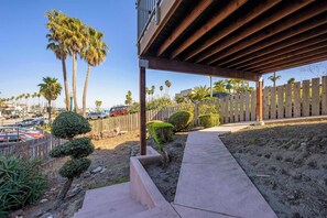 A covered outdoor area with a concrete pathway leading to a wooden deck, surrounded by palm trees and a wooden fence. - Oceanfront Beach House overlooking the Boardwalk (Santa Cruz)