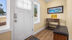 A hotel entrance with a white door, a small wooden bench, a framed picture on the wall, and a sign on the wall. - Oceanfront Beach House overlooking the Boardwalk (Santa Cruz)