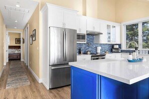 A modern kitchen with stainless steel appliances, white cabinetry, and a blue accent wall. - Oceanfront Beach House overlooking the Boardwalk (Santa Cruz)