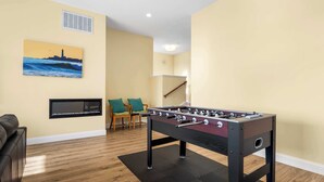 A room with a foosball table, a television, a painting of a lighthouse, and a staircase. - Oceanfront Beach House overlooking the Boardwalk (Santa Cruz)