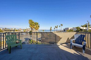 A balcony with two Adirondack chairs facing a beach, a metal fence, and a clear blue sky. - Oceanfront Beach House overlooking the Boardwalk (Santa Cruz)