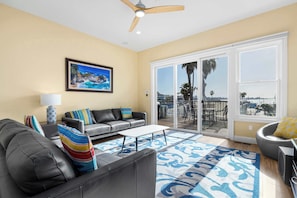 A living room with a sofa, a coffee table, a painting, and a view of the outdoors through large sliding doors.