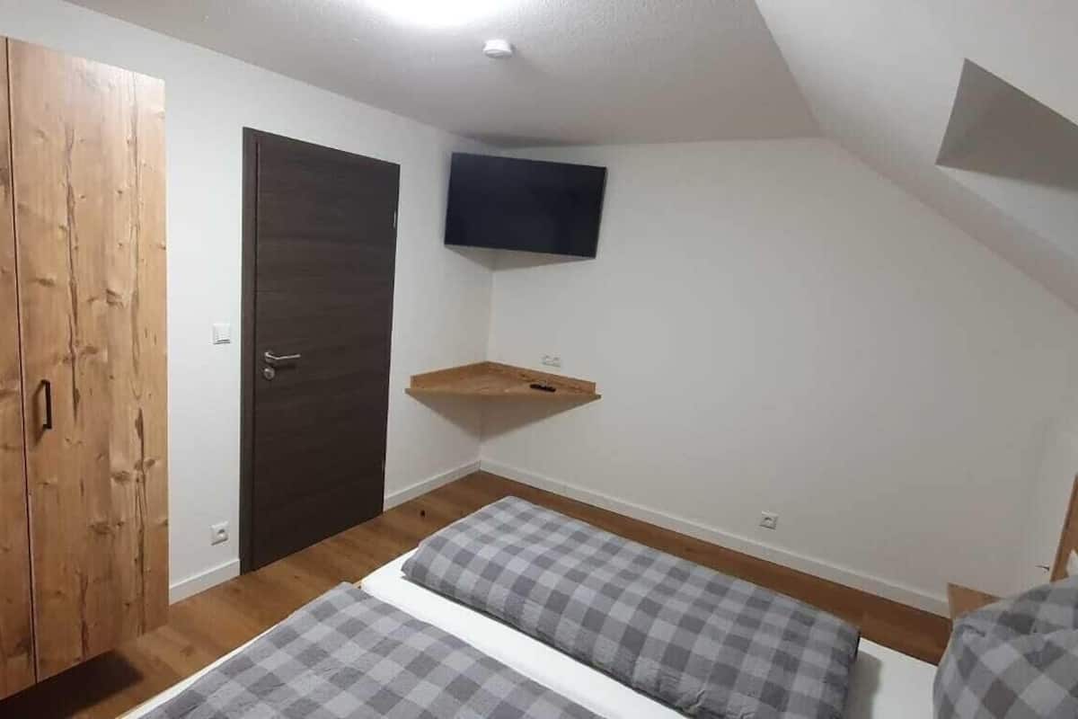 A bedroom with a wardrobe, a bed, a television mounted on the wall, and a small shelf.