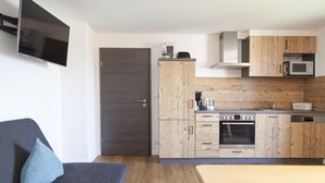 A compact living space with a sofa, a flat-screen TV, a kitchenette with wooden cabinets, a microwave, and a built-in oven. - Stadl Appartements (Tuerkheim)