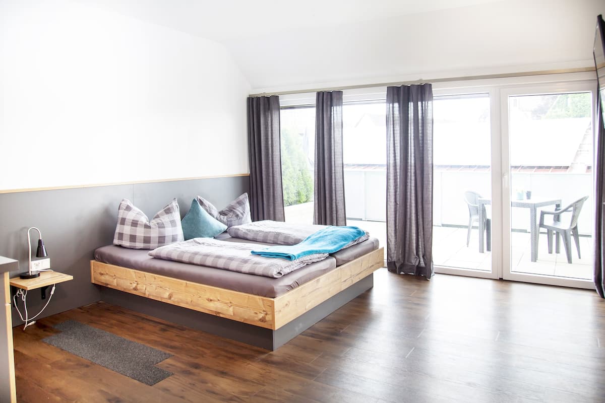 A modern bedroom with a wooden bed, grey curtains, and a view of the outdoors.