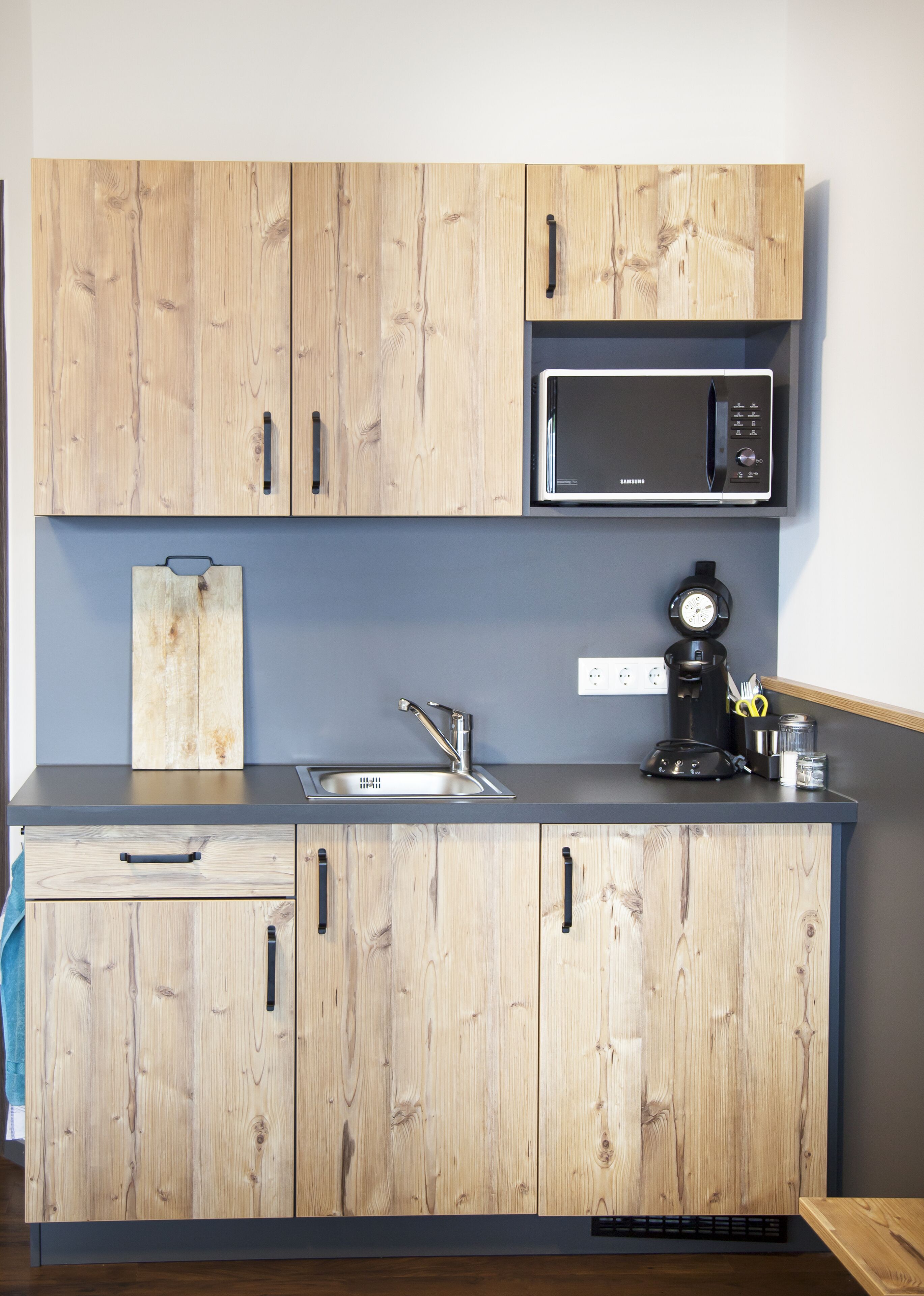 A kitchen with wooden cabinets, a stainless steel sink, a microwave, and a coffee maker.