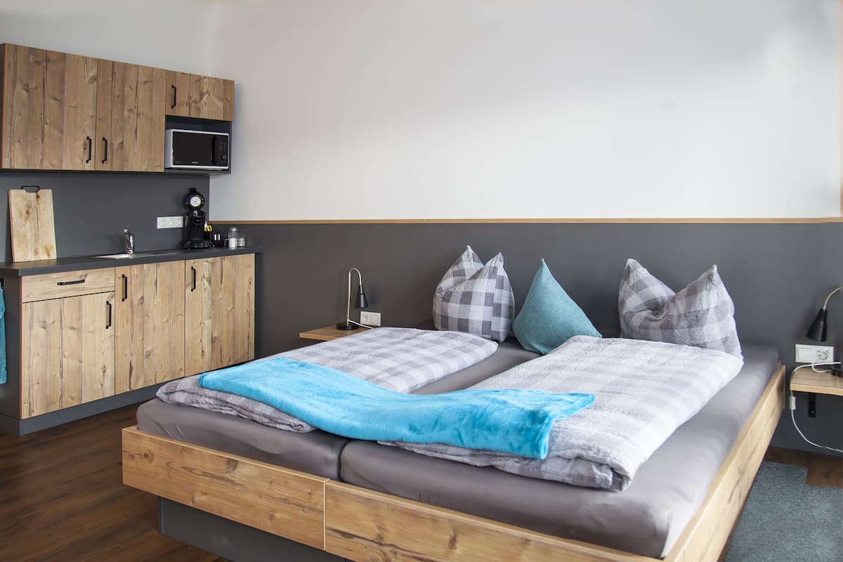 A modern bedroom with a wooden bed frame, a built-in desk, a microwave, and a small bedside table.