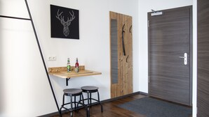 A modern room with a wooden floor, a small bar area with stools, a wall-mounted deer head artwork, a wooden door, and a gray doormat. - Stadl Appartements (Tuerkheim)