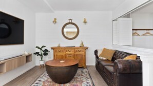 A modern living room with a round wooden coffee table, a brown leather sofa, a wooden cabinet, and a large mirror on the wall. - Skippers Landing- On the water with private jetty (Lemon Tree Passage)