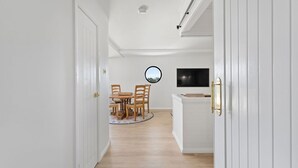 A hallway leading to a dining area with a round mirror, a TV mounted on the wall, and a white cabinet with a gold handle. - Skippers Landing- On the water with private jetty (Lemon Tree Passage)