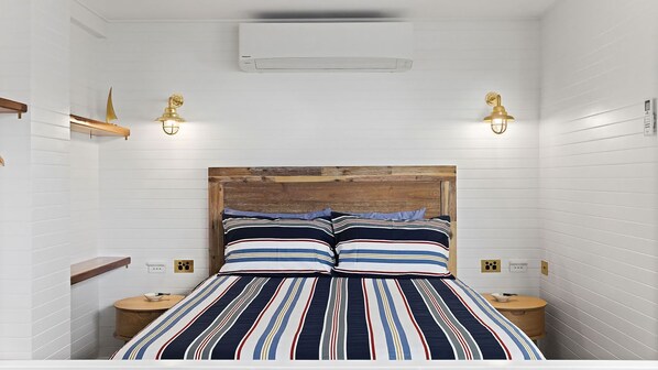 A bedroom with a wooden headboard, striped bedding, two bedside tables, and wall-mounted lights. - Skippers Landing- On the water with private jetty (Lemon Tree Passage)