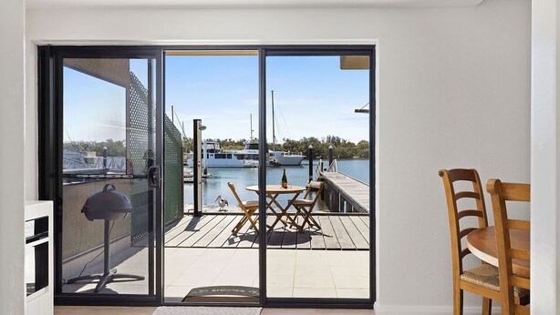 A sliding glass door leading to an outdoor deck with a view of a marina and boats. - Skippers Landing- On the water with private jetty (Lemon Tree Passage)