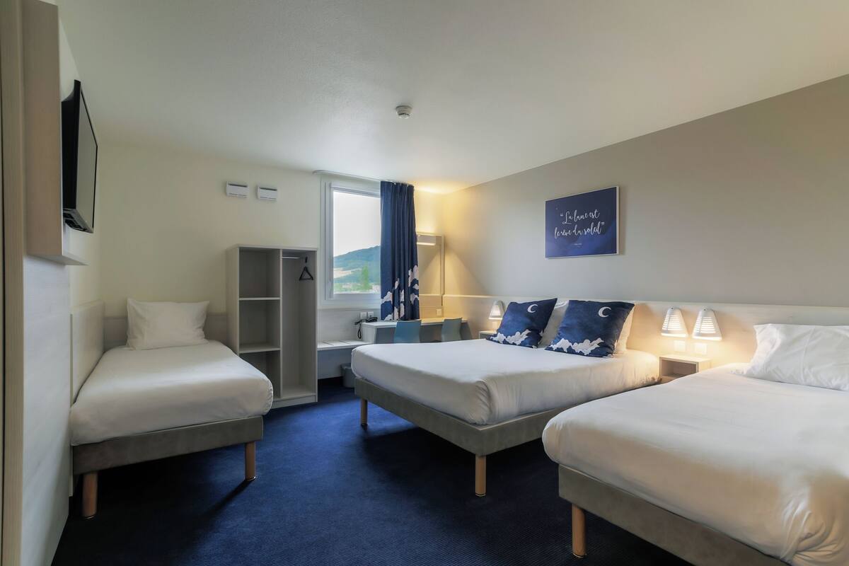 Une chambre d’hôtel avec deux lits simples, un bureau, une armoire et une fenêtre donnant sur un paysage agréable.
