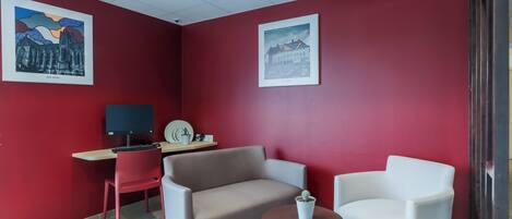 A room with red walls, a desk with a computer, two chairs, and a small table with a plant.