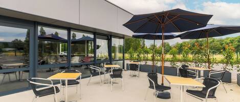 An outdoor patio with tables and chairs, large umbrellas, and a view of greenery and buildings.
