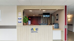A hotel reception desk with a wooden counter, a potted plant, and a digital screen. - ACE Hôtel Thionville Porte du Luxembourg (Thionville)