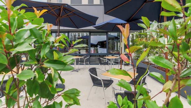 An outdoor seating area with tables and chairs, umbrellas, and greenery. - ACE Hôtel Thionville Porte du Luxembourg (Thionville)