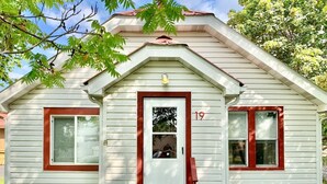Une maison de plain-pied avec une porte rouge, deux fenêtres aux encadrements rouges et le numéro « 19 » sur la porte.