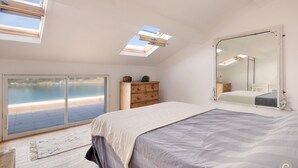 Ein Schlafzimmer mit einem großen Bett, einem Schminktisch, einem Spiegel und Meerblick durch eine Schiebetür.