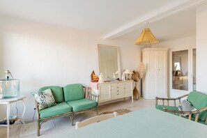 Une pièce avec un canapé vert, une armoire blanche, un miroir et une lampe suspendue.