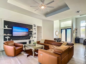 A modern living room with a large flat-screen TV, leather sofas, a coffee table, and decorative items on shelves.