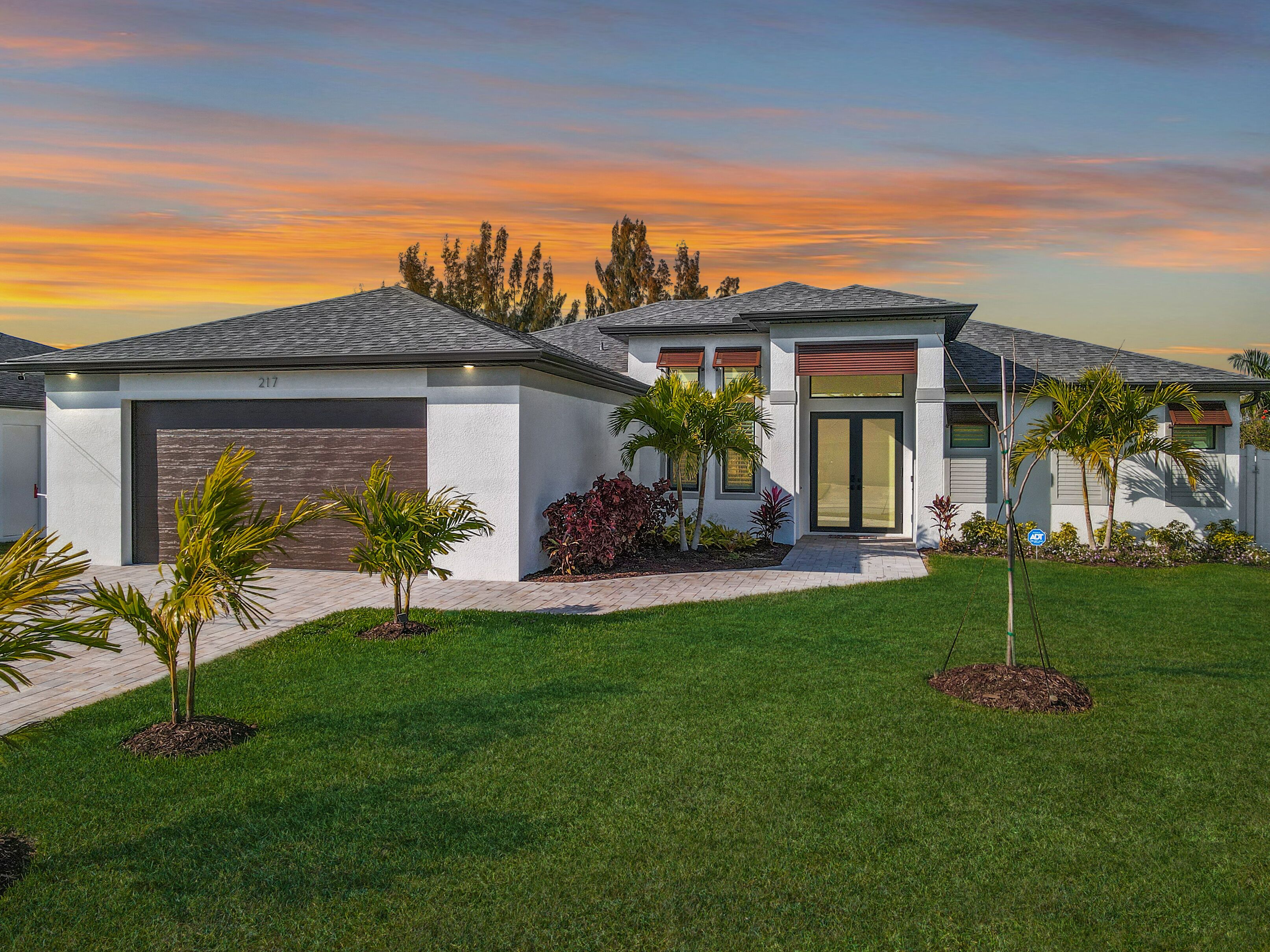 A modern two-story house with a garage, a well-maintained lawn, and a variety of plants.