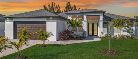 A modern two-story house with a garage, a well-maintained lawn, and a variety of plants.