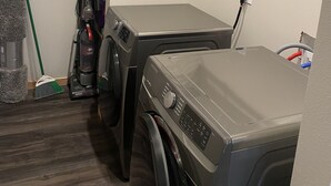 A laundry room with two front-loading washing machines, a vacuum cleaner, and a broom. - Brand New Duplex Across the road from Devils Lake w/lake access (Warwick)