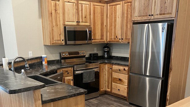 A modern kitchen with wooden cabinets, stainless steel appliances, and a granite countertop. - Brand New Duplex Across the road from Devils Lake w/lake access (Warwick)