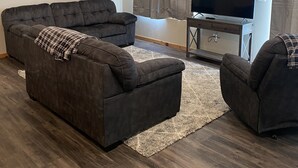 A living room with a sectional sofa, a TV, and a small table. - Brand New Duplex Across the road from Devils Lake w/lake access (Warwick)
