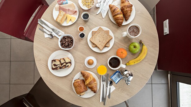 Una mesa redonda con alimentos para el desayuno, como cruasanes, pan, frutas y café.