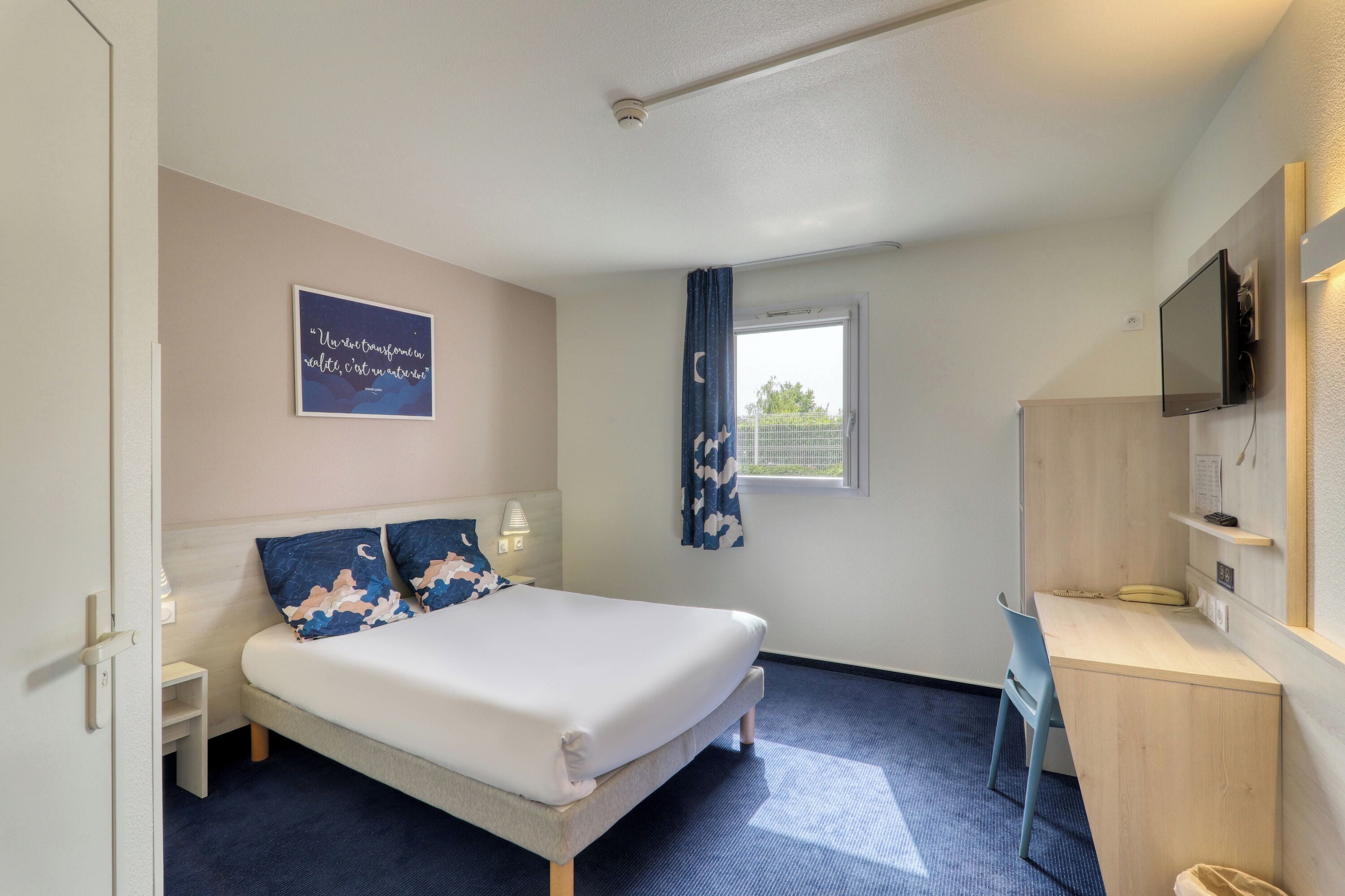 Habitación de hotel con cama, escritorio y ventana con cortinas.