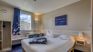 Habitación de hotel con cama, mesitas de noche, ventana con vistas, un banco empotrado y una obra de arte en la pared.