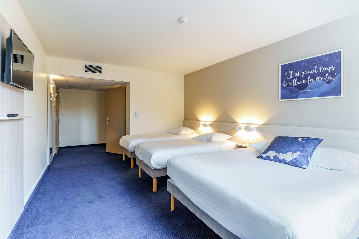 Habitación de hotel con tres camas individuales, un televisor y una frase inspiradora en la pared.