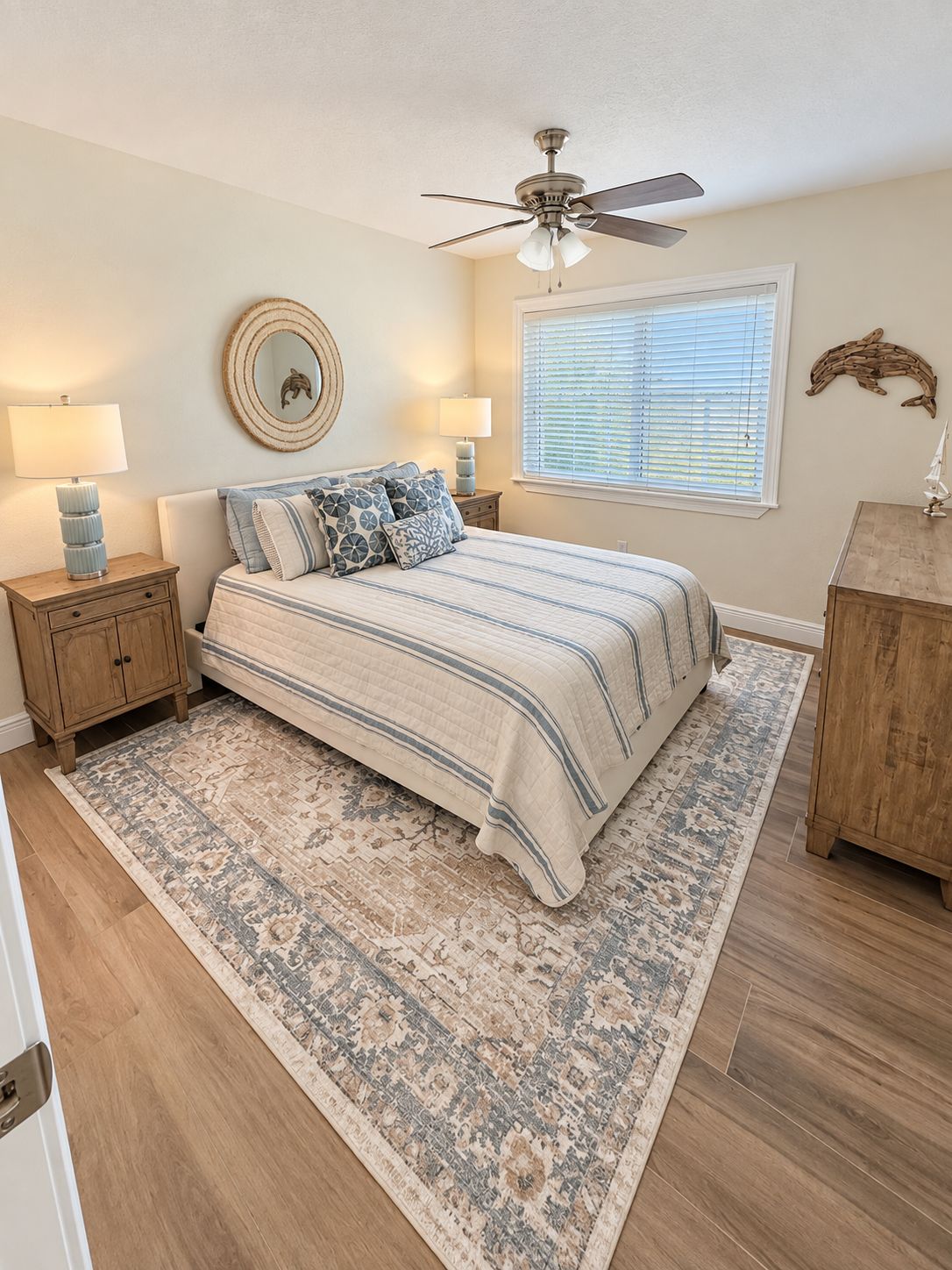 A bedroom with a bed, two bedside tables, a ceiling fan, a window with blinds, and a decorative wall piece.