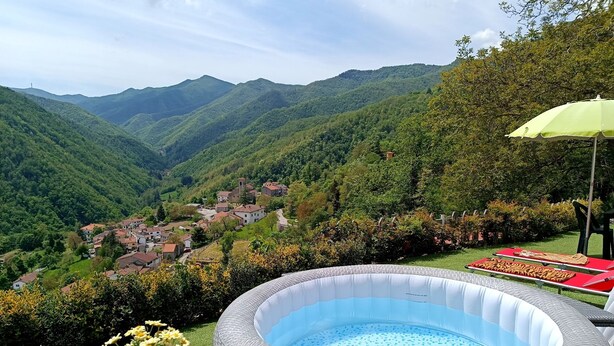 A hot tub surrounded by a garden with yellow flowers, a green umbrella, and a view of a village in the valley. - Romantic house with swimming pool near Bologna & Florence CIN: IT047018C2OXJNJAB8 (Treppio)