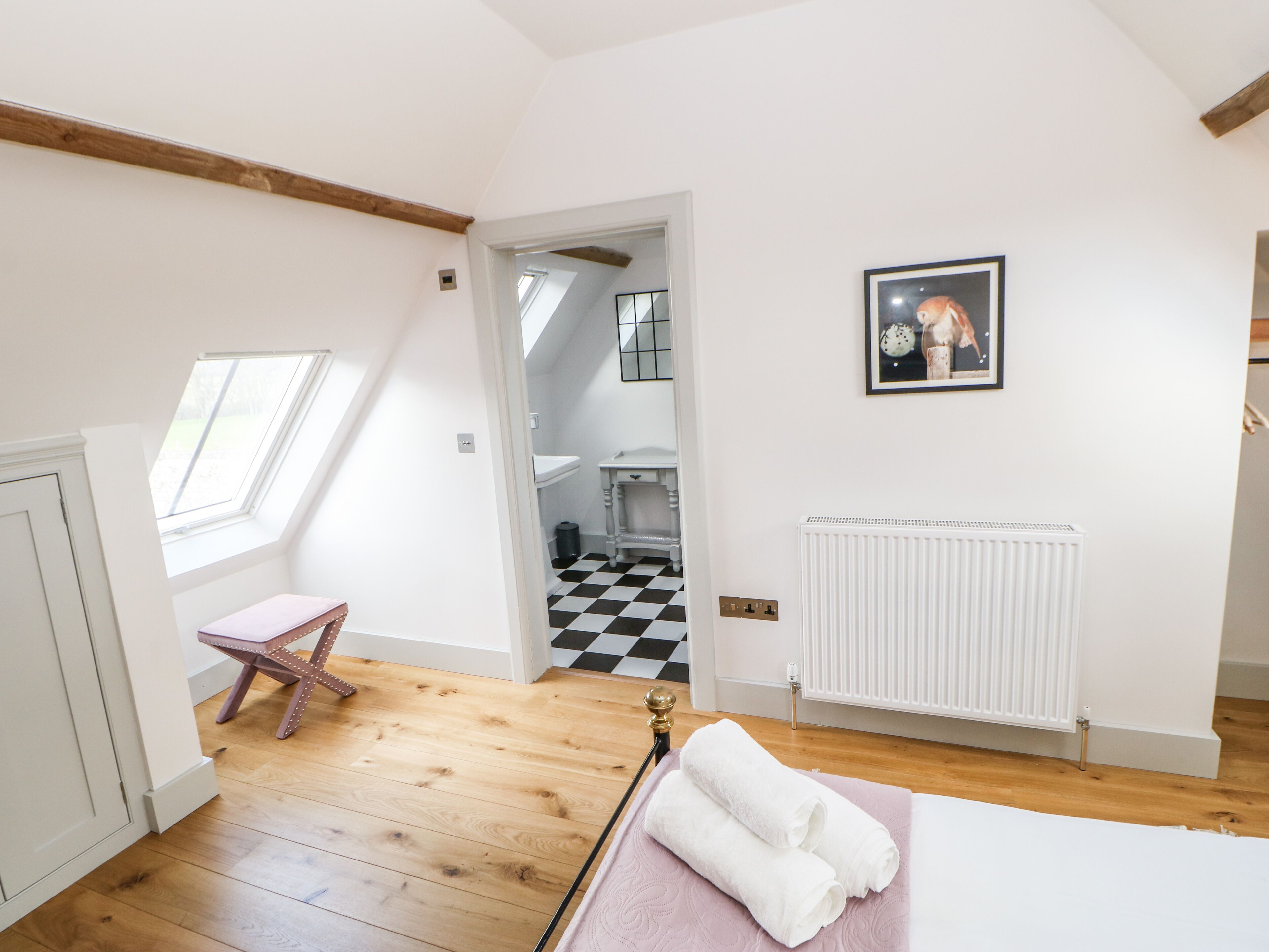 A room with a sloped ceiling, a skylight, a white radiator, a checkered floor, and a framed picture on the wall.