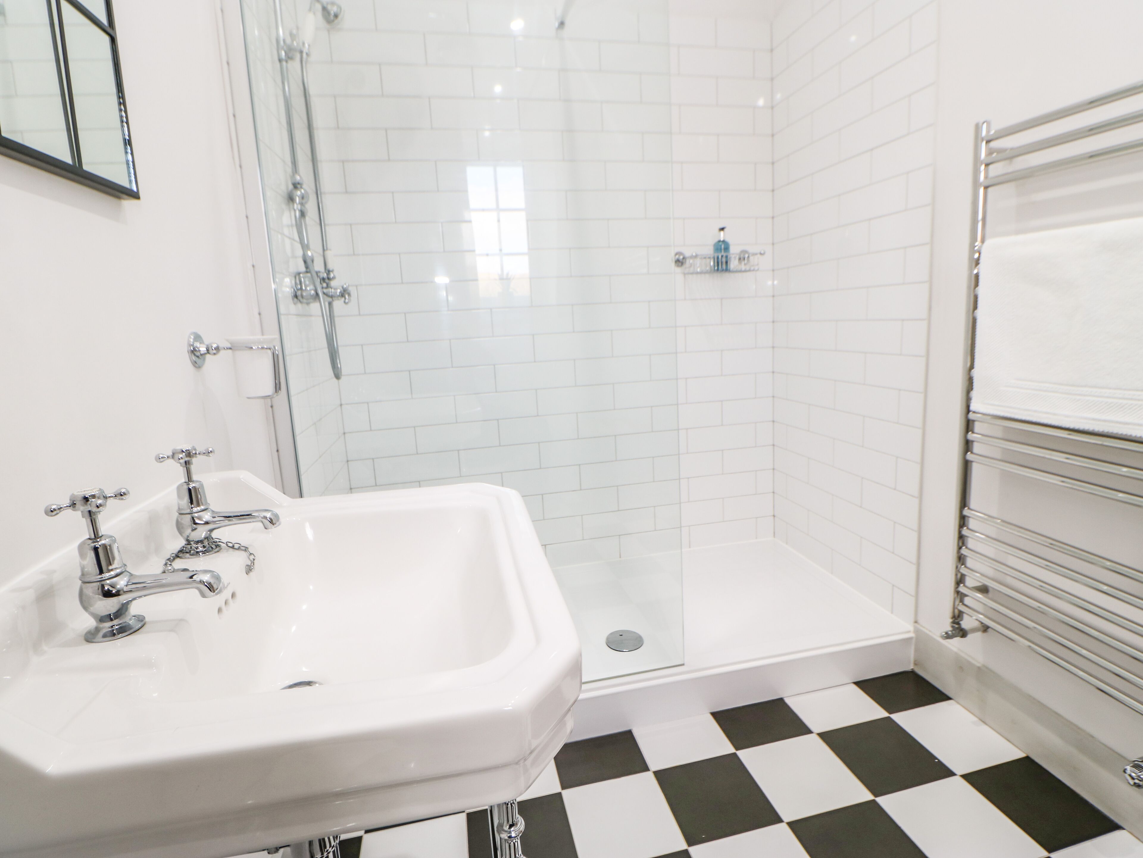 A bathroom with a white sink, a shower, and a checkered floor.