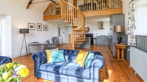 Un vaste espace de vie avec un canapé bleu, un escalier en bois et une cuisine en arrière-plan.