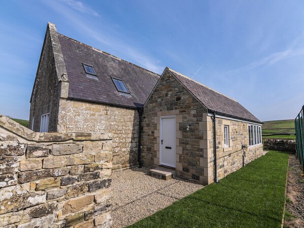 A stone farmhouse with a sloped roof, a small porch, and a gravel driveway.