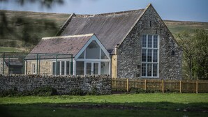 Une maison en pierre avec un toit à pignon, une clôture en bois et un mur de pierre à l’avant.