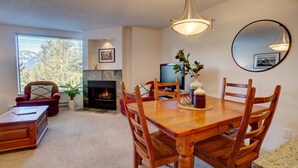 A dining area with a wooden table and chairs, a fireplace, and a television in the background. - Mountainside 1BR: Sleeps 4, Pool, Hot tub & Private Balcony - Walk to Everything! (Whistler)