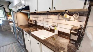 Una cocina compacta con armarios blancos, encimera de granito, horno integrado y cafetera.