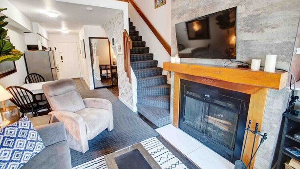 Una sala de estar moderna con chimenea, un televisor montado encima y una escalera que sube a un nivel superior.