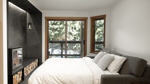 A bedroom with a bed, a fireplace, a sofa, and a window with a view of trees.