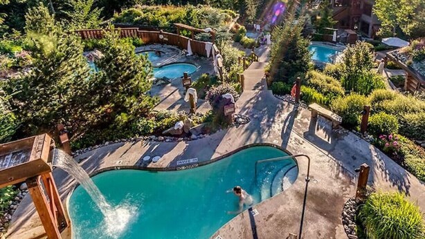 A resort with multiple swimming pools surrounded by lush greenery and mountains in the background.